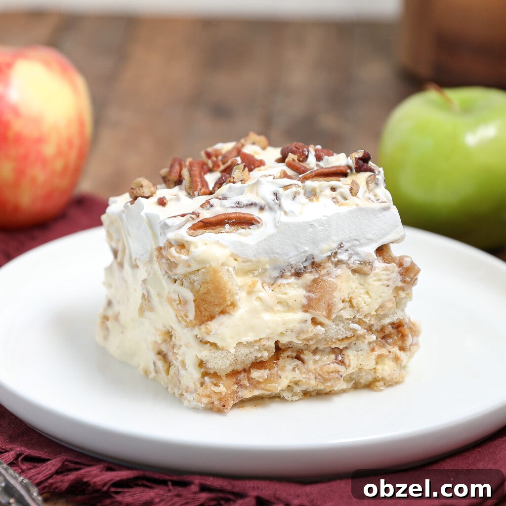 Caramel Apple Tiramisu Recipe: Autumn Dessert Twist 7 A slice of creamy caramel apple tiramisu with whipped topping and chopped pecans sits on a white plate. A red apple and a green apple are in the background on a rustic wooden surface.