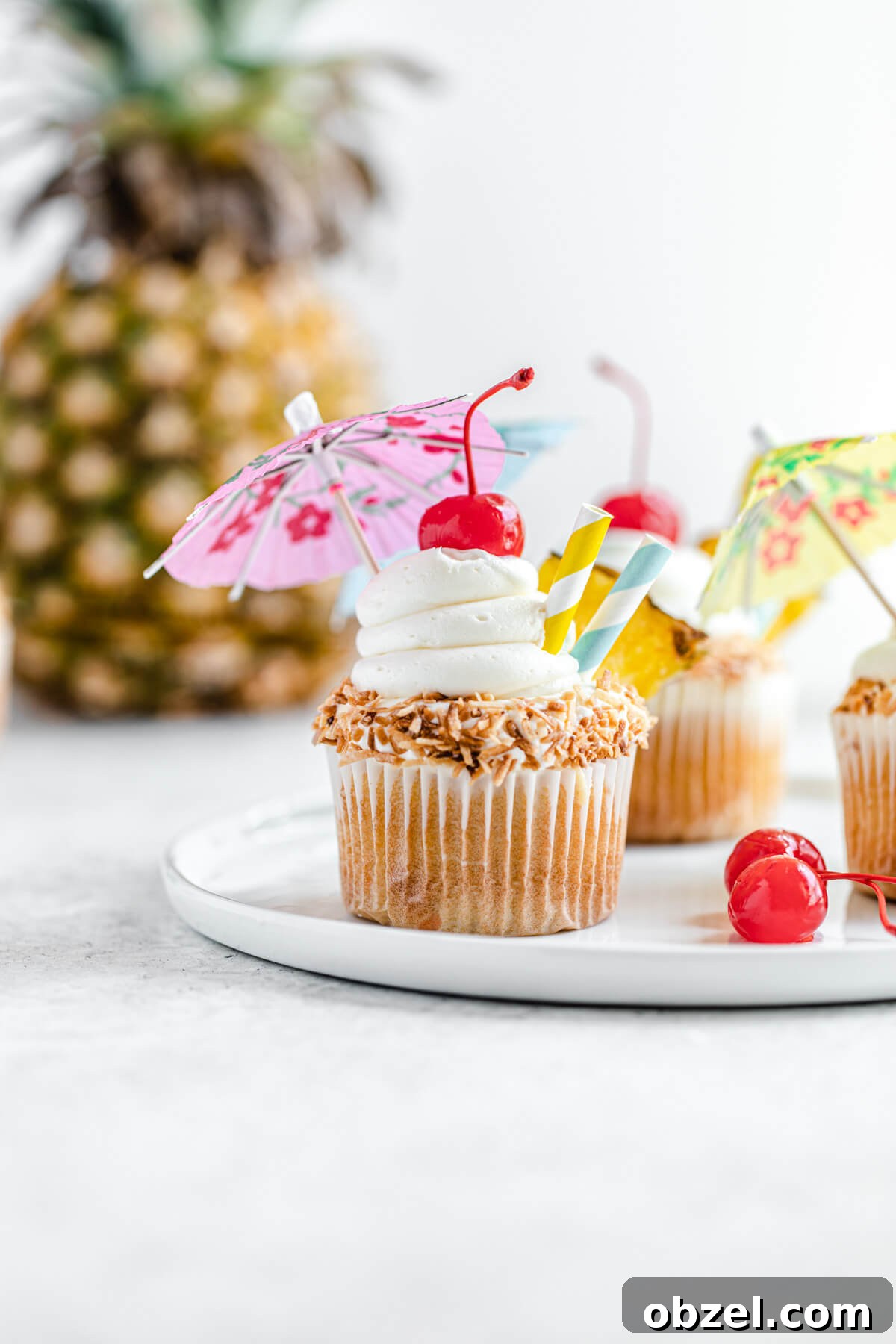 Pina Colada Cupcakes with Rum Infused Coconut Frosting 7 cupcake topped with umbrellas on a white plate with pineapple behind them