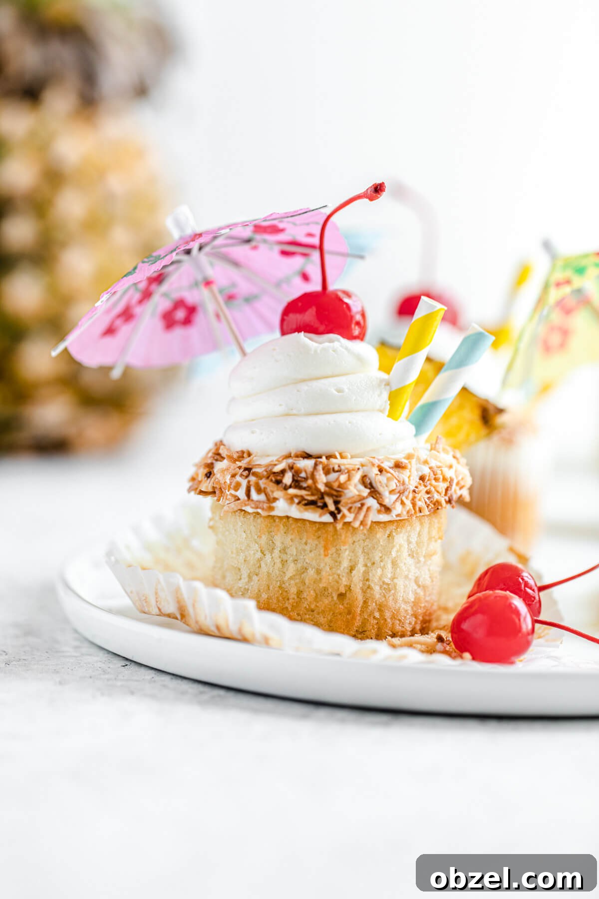Pina Colada Cupcakes with Rum Infused Coconut Frosting 8 unwrapped cupcake on a white plate with pineapple in the background