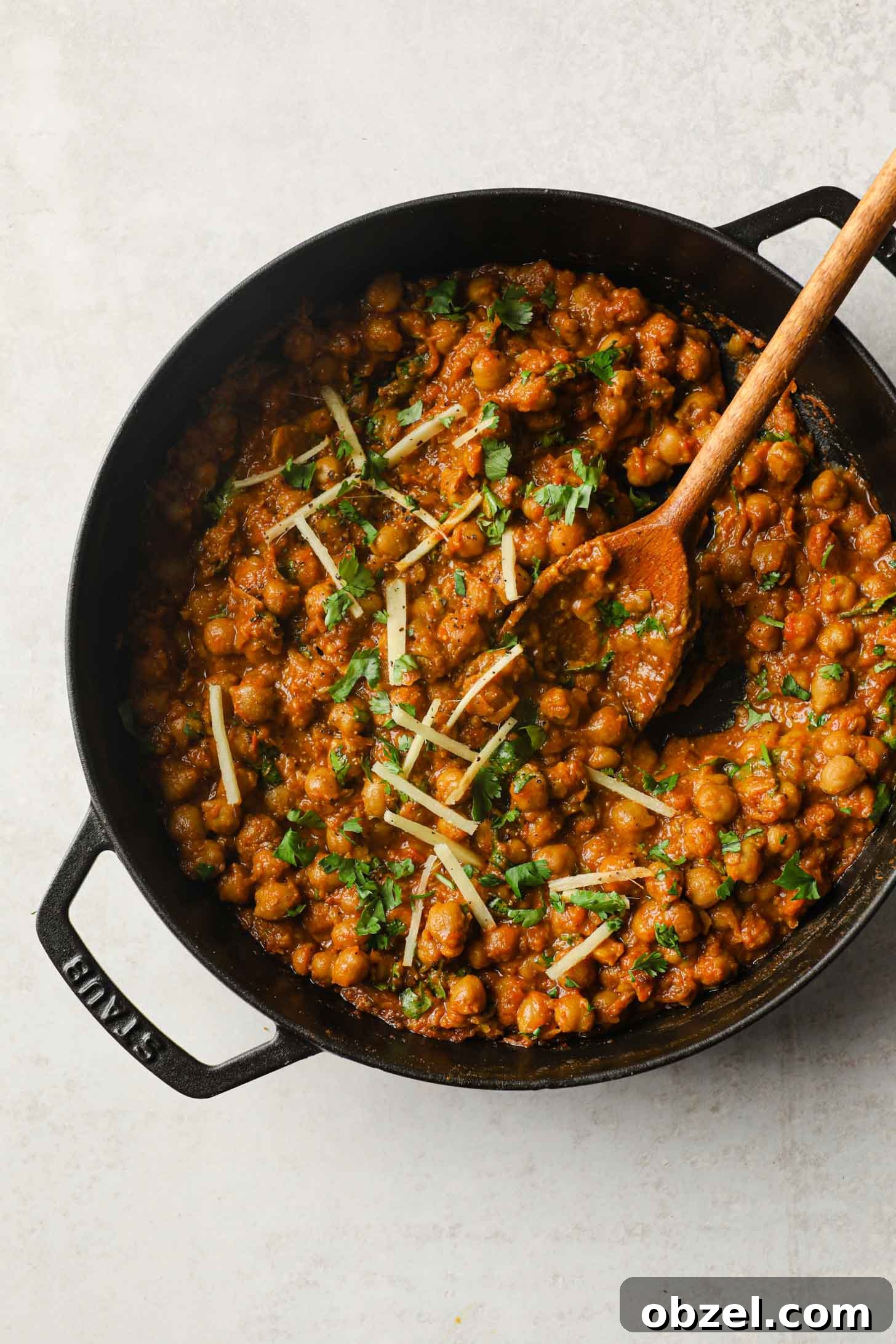 Chickpea Curry inside in a black skillet with a wooden spoon