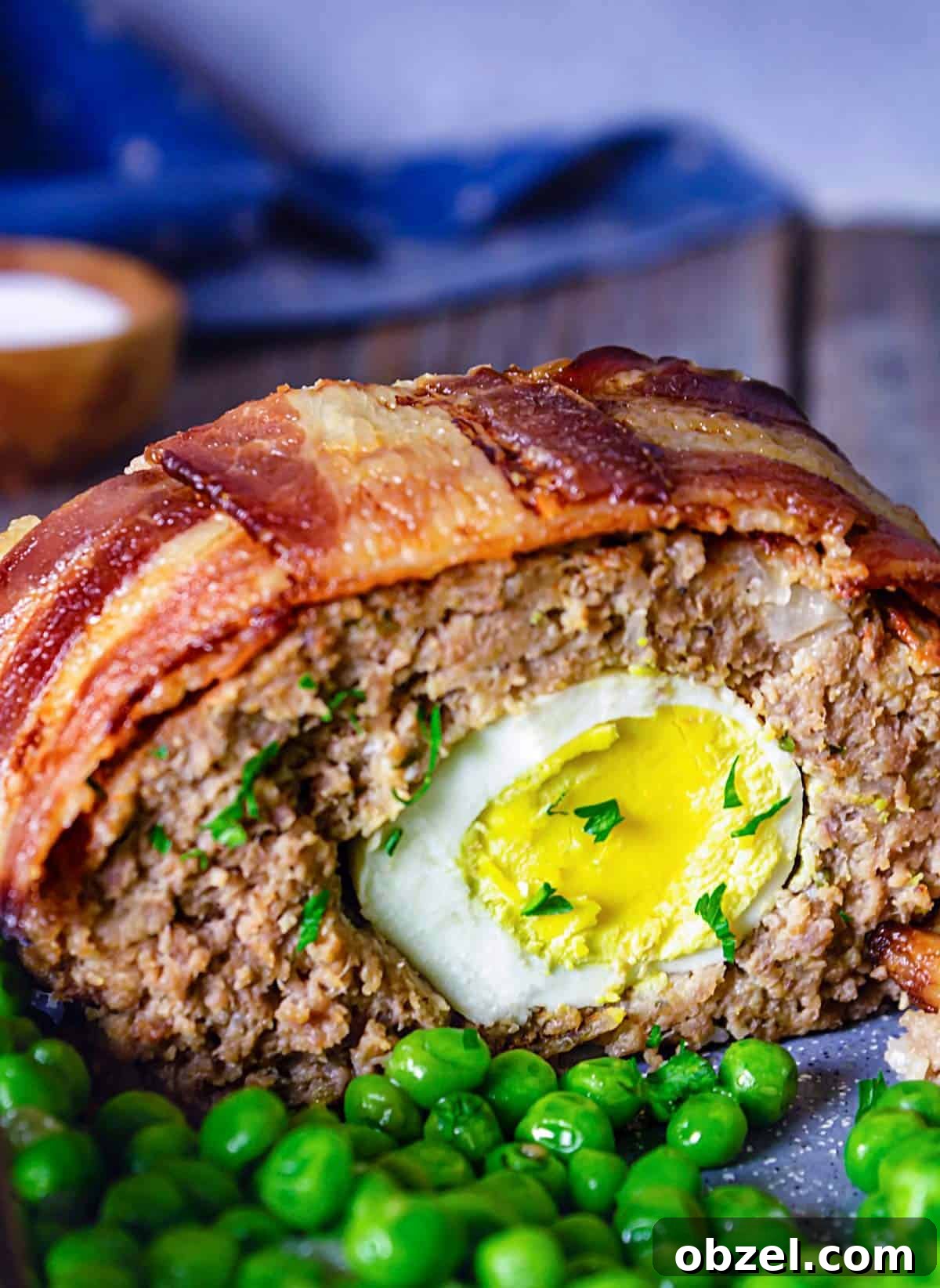 A close up of the sliced meatloaf with bacon on top and cooked egg in the middle with a side of peas.