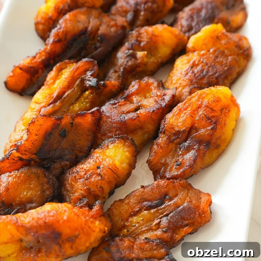Crispy Fried Maduros (Sweet Plantains Recipe) 2 Golden brown fried plantains with crispy edges on a plate.