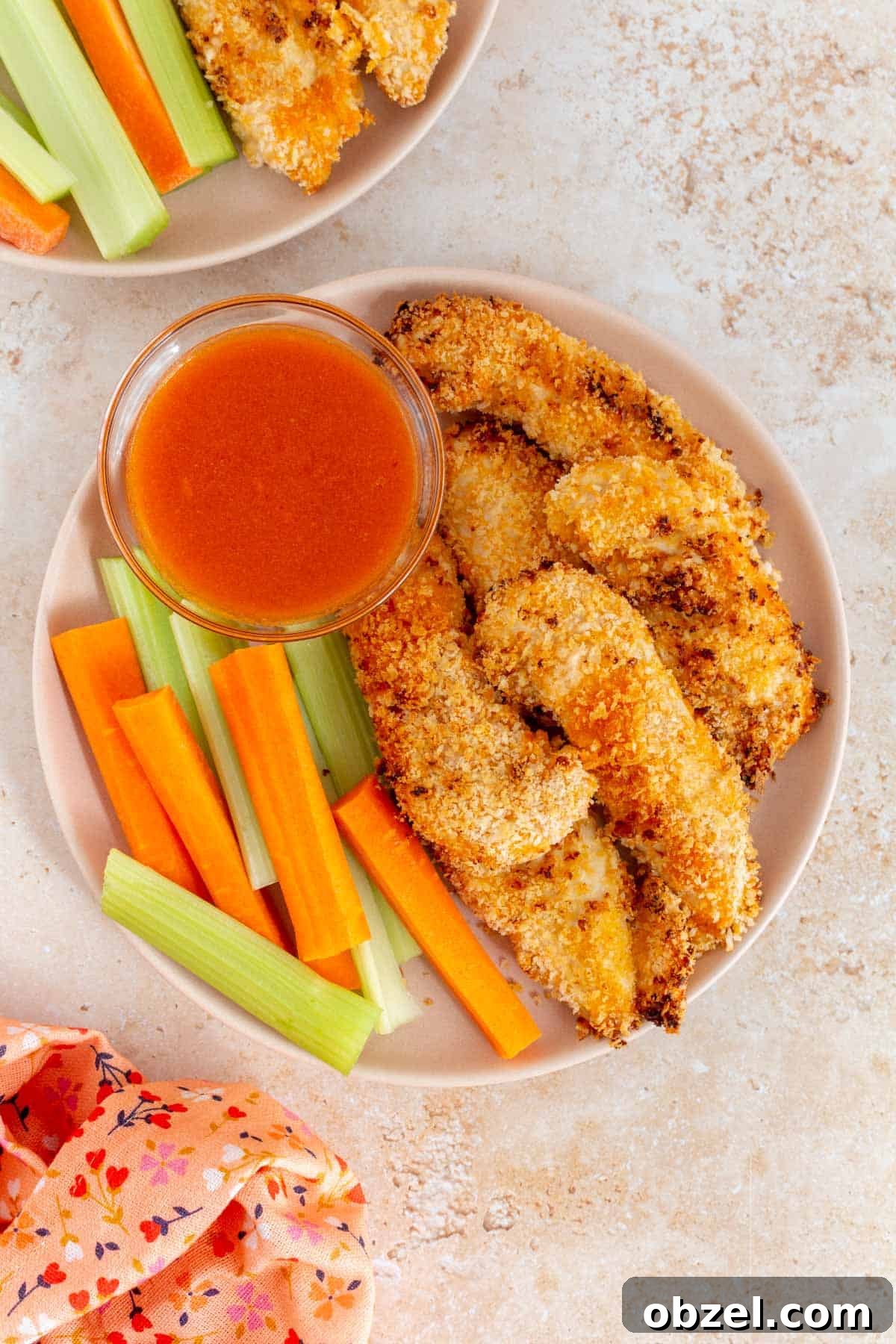 Crispy Air Fryer Buffalo Chicken Tenders 2 Overhead view of a plate of air fryer buffalo chicken tenders with carrots and celery along with a bowl of buffalo sauce.