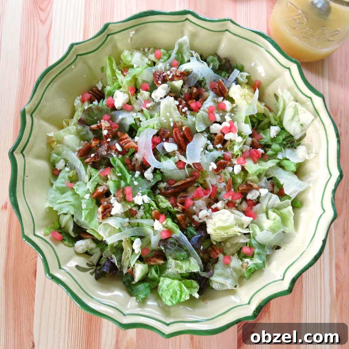 Bowl of summer salad with fennel, watermelon, feta, and candied pecans with a jar of Orange honey mustard vinaigrette in a mason jar behind it.
