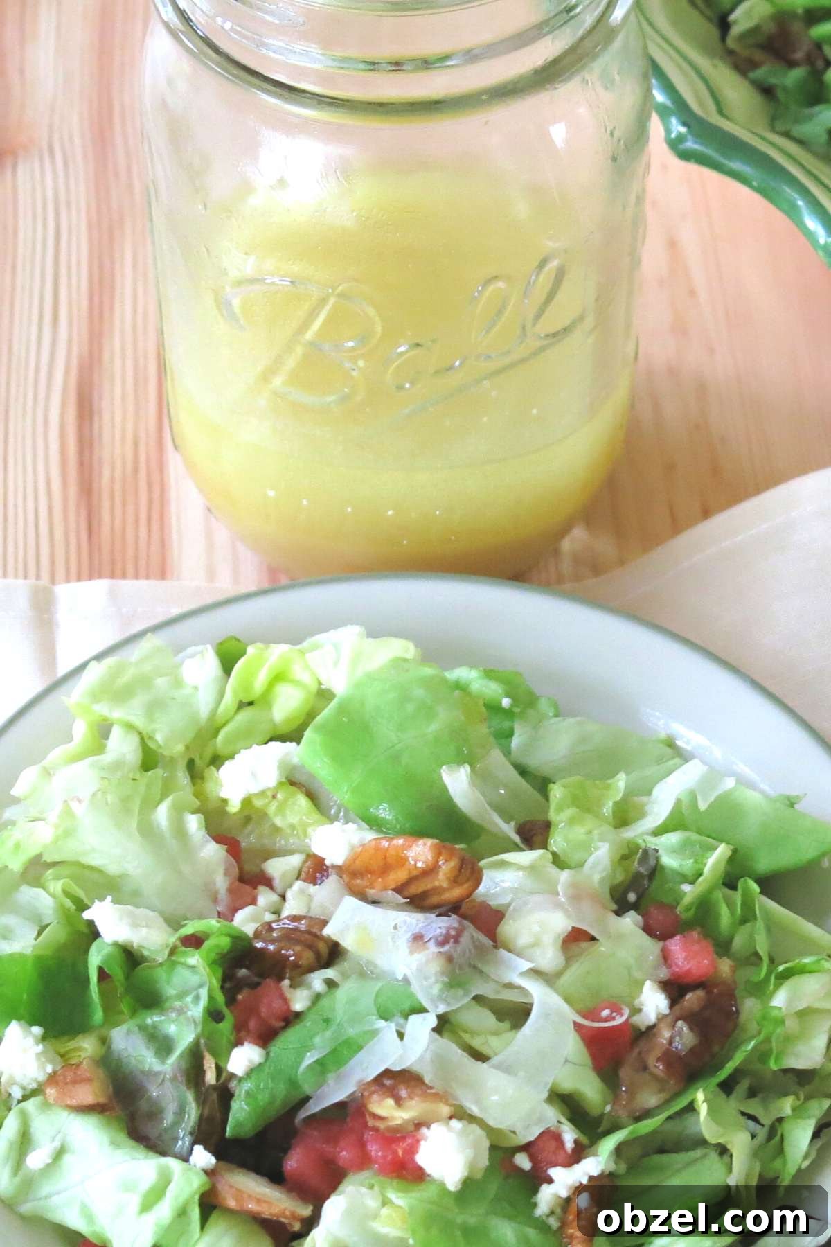 Orange honey mustard vinaigrette in a mason jar with a plate of summer salad with fennel, watermelon, feta, and candied pecans in front of it.