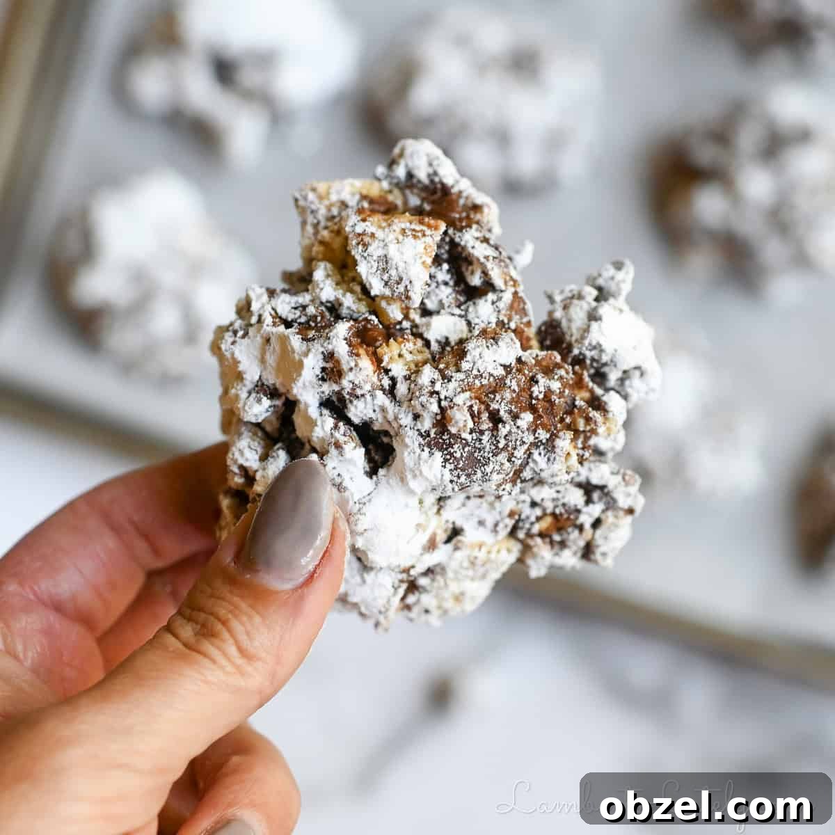 No Bake Muddy Buddy Cookies 2 holding a muddy buddies cookie in front of a baking sheet full of cookies.