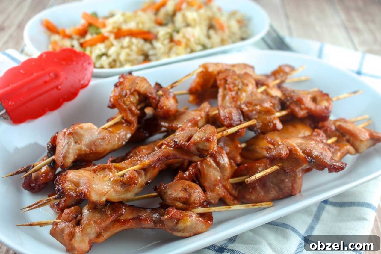 15 Air Fryer Chicken Thigh Recipes for Crispy, Juicy Results 14 Skewers of teriyaki chicken piled on a white serving platter with rice side dish in background.