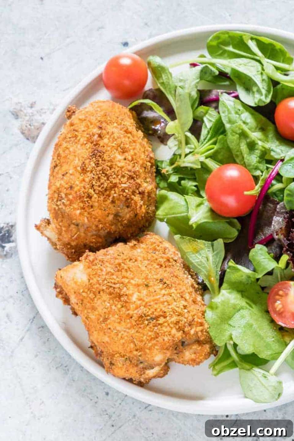 15 Air Fryer Chicken Thigh Recipes for Crispy, Juicy Results 16 Two Crispy Chicken Thighs on a white plate next to tossed salad.