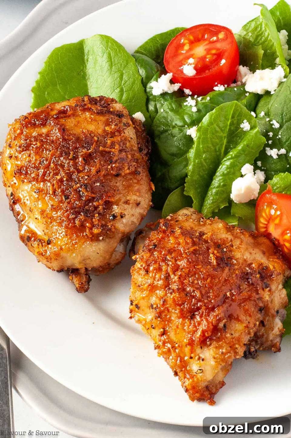 15 Air Fryer Chicken Thigh Recipes for Crispy, Juicy Results 5 Two thighs on white dinner plate with tomato and feta salad along side.