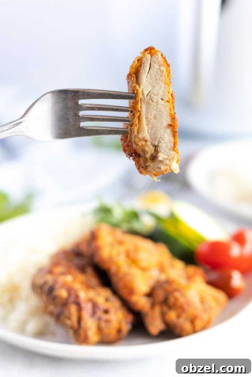 15 Air Fryer Chicken Thigh Recipes for Crispy, Juicy Results 8 Fork lifting one bite of chicken, with dinner plate of two thighs, rice and veggies in background.