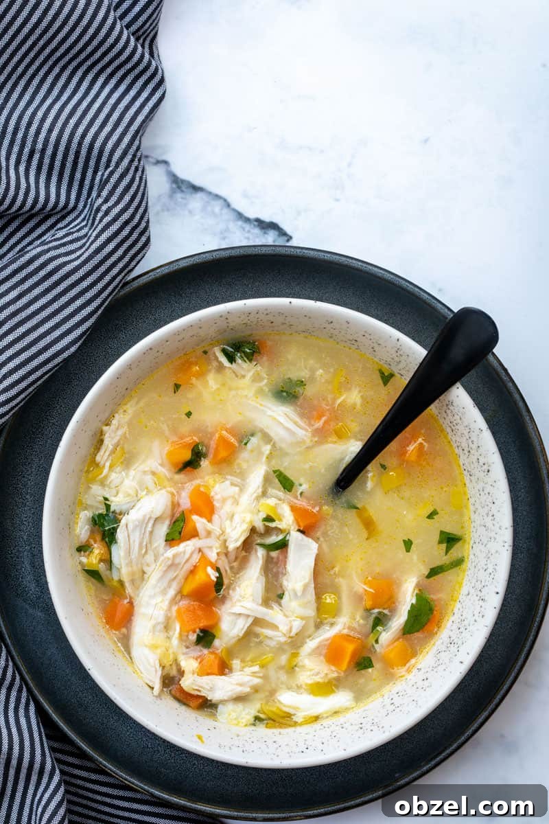 bowl of chicken soup with rice and lemon next to striped napkin