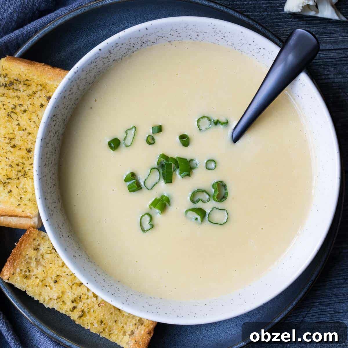 bowl of cauliflower leek potato soup topped with scallions next to slices of garlic bread.