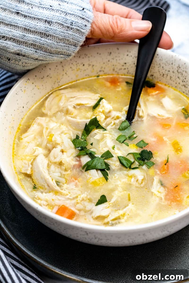 close up on bowl of chicken soup with rice with hand holding spoon