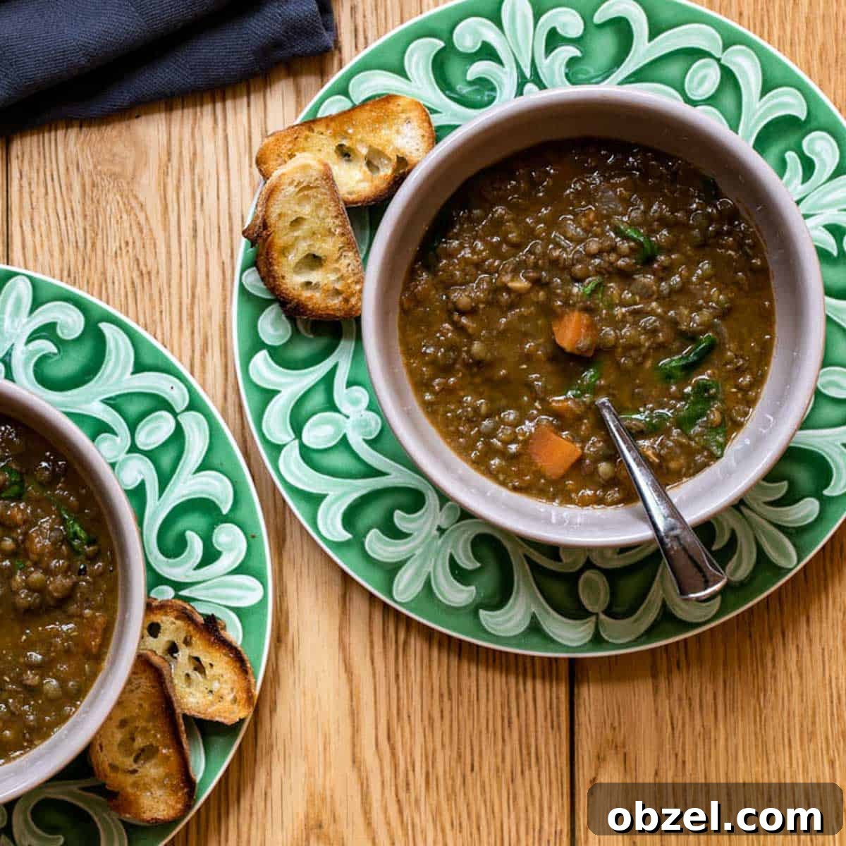 two bowls of French lentil soup on plates with baguette toasts.