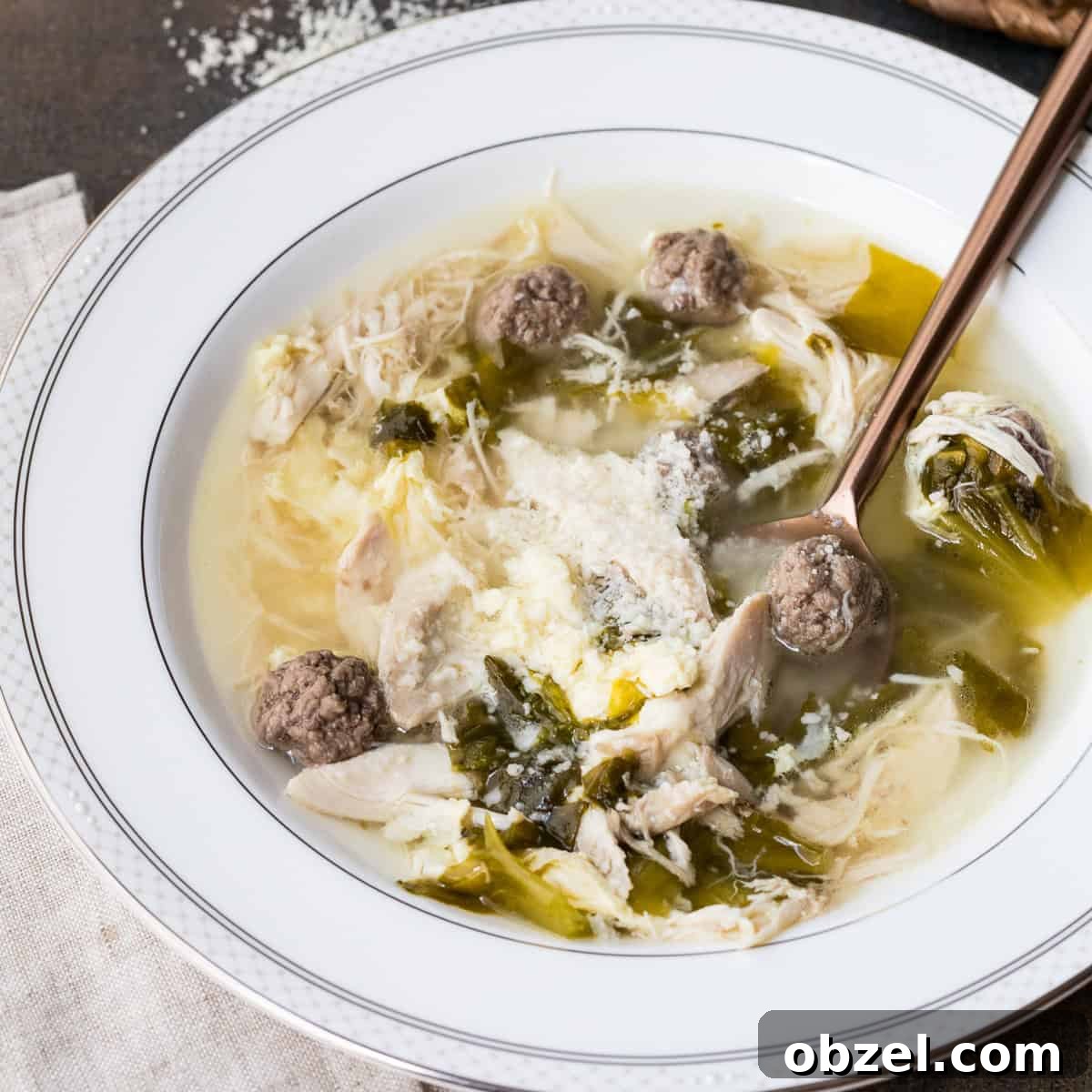bowl of italian wedding soup with spoon, sprinkled with parmesan cheese.