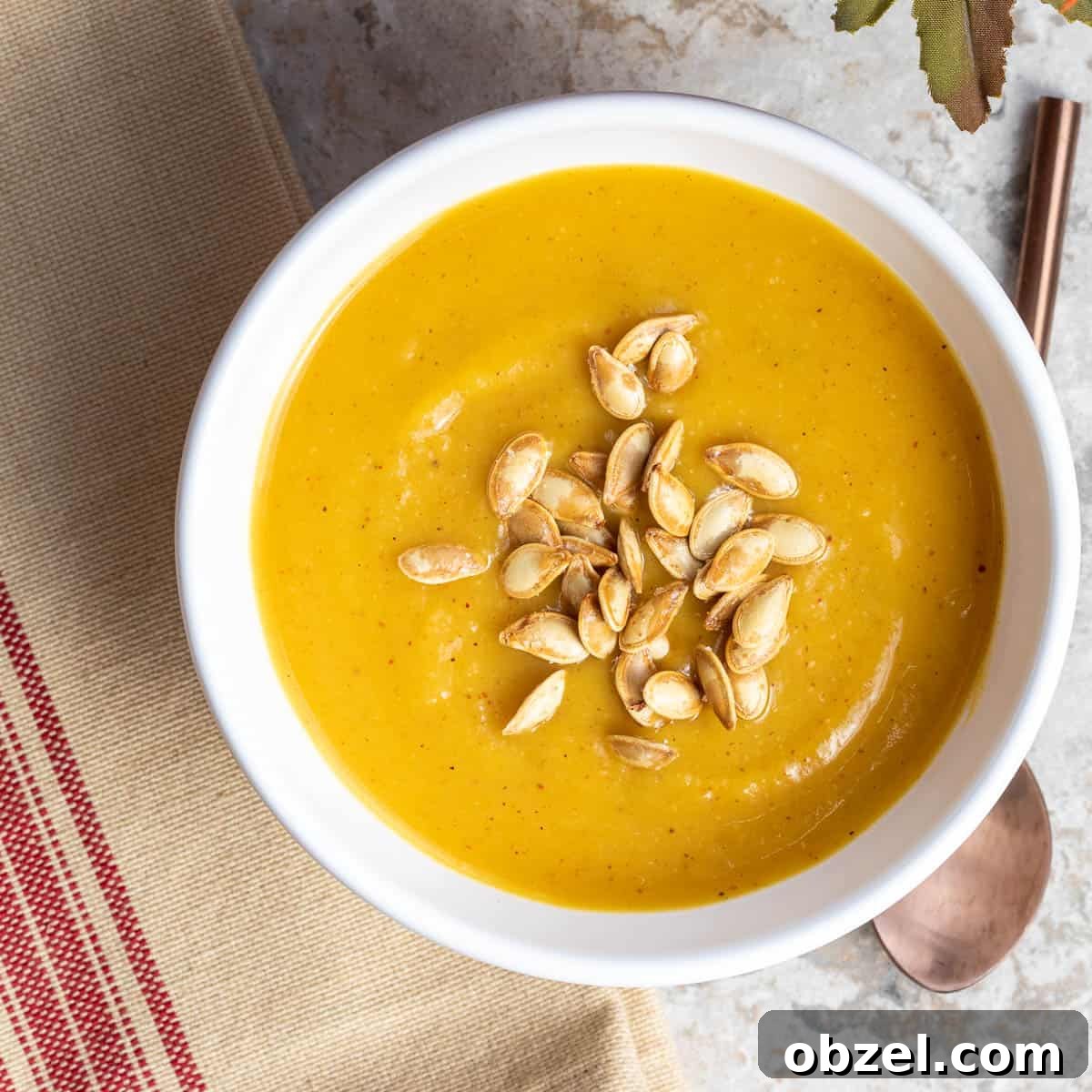 pumpkin soup without cream topped with pumpkin seeds next to napkin and spoon