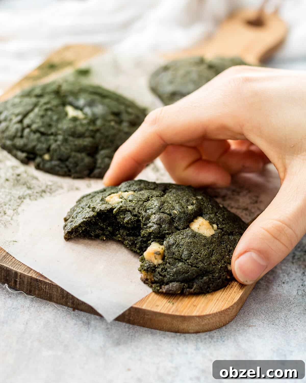 Spirulina Cookies Recipe with a Vibrant Green Superfood Twist 2 Three Spirulina Cookies on a wooden chopping board. A bite has been taken from the front cookie and there is a hand holding it.