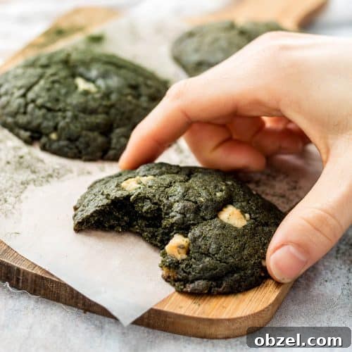 Spirulina Cookies Recipe with a Vibrant Green Superfood Twist 4 Three Spirulina Cookies on a wooden chopping board. A bite has been taken from the front cookie and there is a hand holding it.