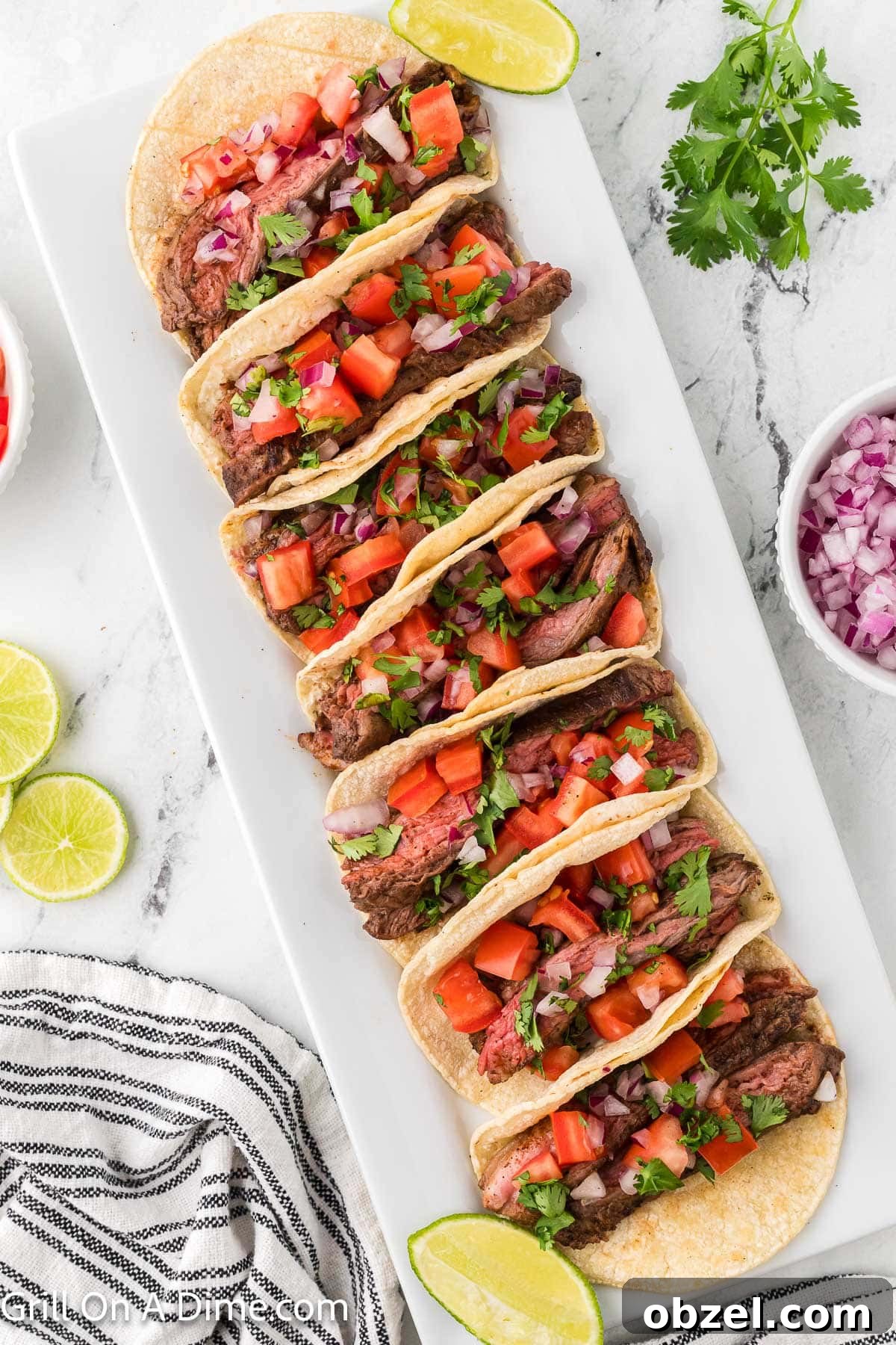 Juicy Blackstone Steak Tacos with Charred Onions and Lime 10 Steak tacos topped with diced tomatoes, red onions and fresh cilantro on a white platter