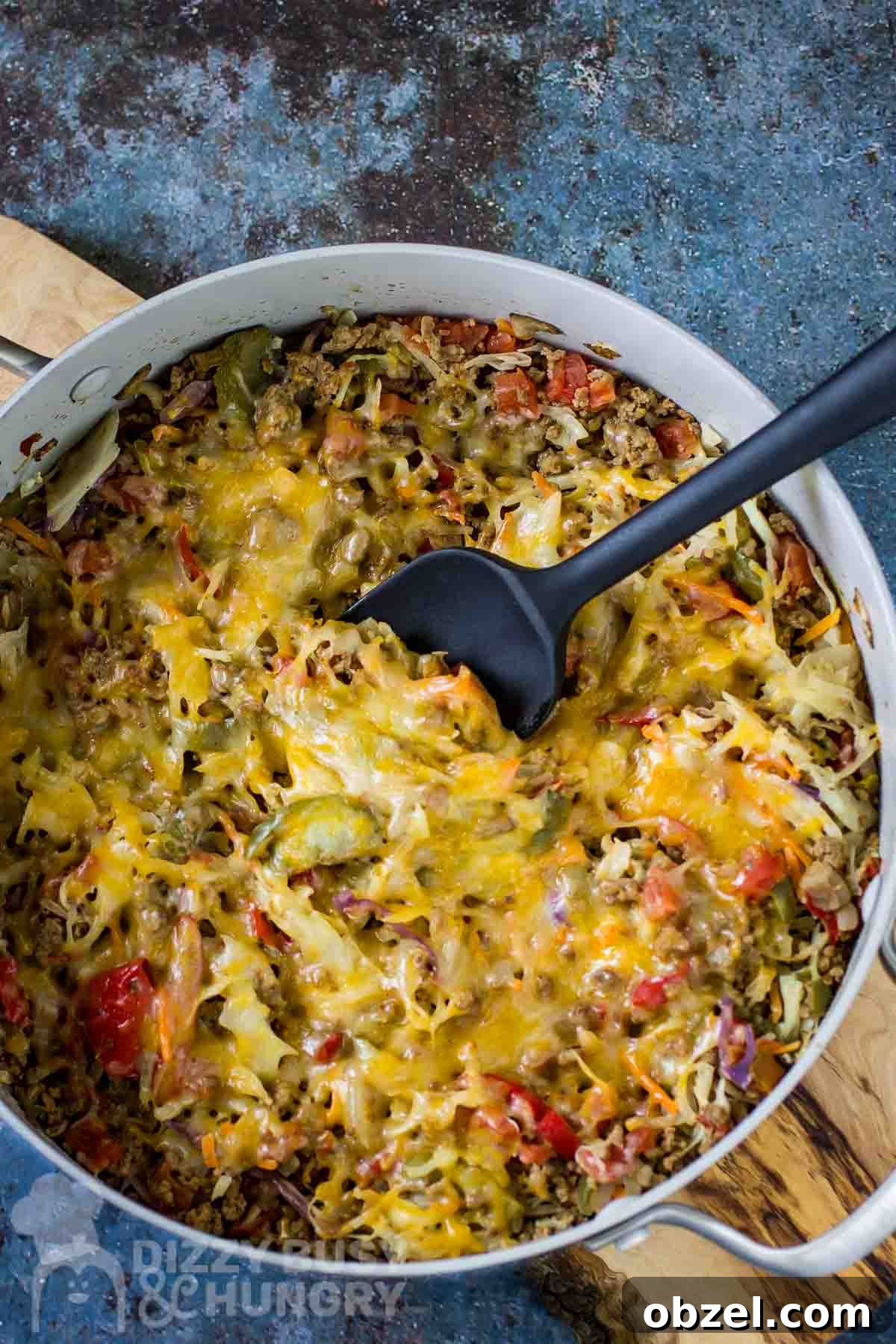 One Skillet Stuffed Cabbage Casserole Recipe 2 Overhead shot of cabbage casserole in a large shallow pot with a black spatula all resting on a wooden surface.