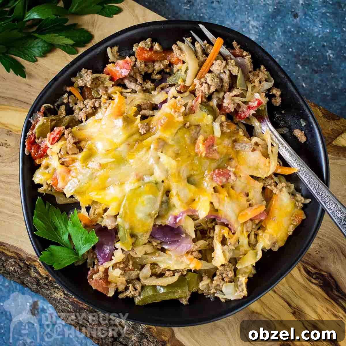 One Skillet Stuffed Cabbage Casserole Recipe 6 Close up overhead shot of cabbage casserole on a black plate with a silver fork on the side all on a wooden cutting board on a blue surface with herbs on the side.