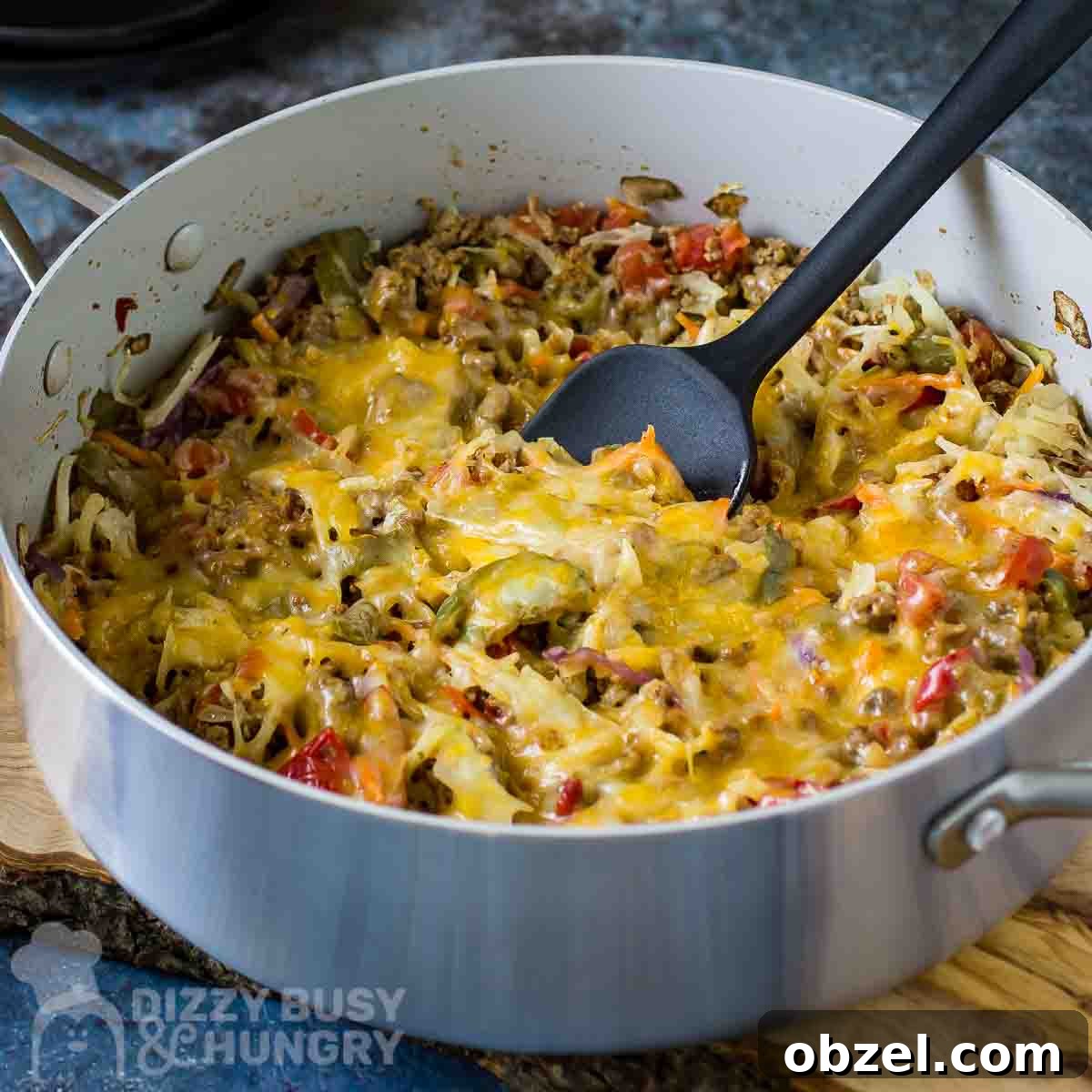 One Skillet Stuffed Cabbage Casserole Recipe 7 Side angled shot of cabbage casserole in a large shallow pot with a black spatula all resting on a wooden surface.