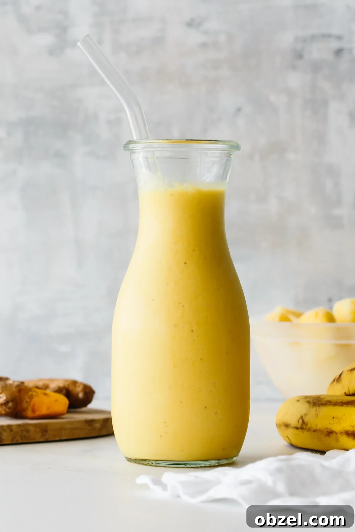 Turmeric smoothie in a glass jar with straw and ingredients in the background.