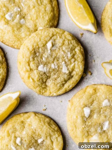 Lemon white chocolate cookies with lemon slices in between on white parchment paper.