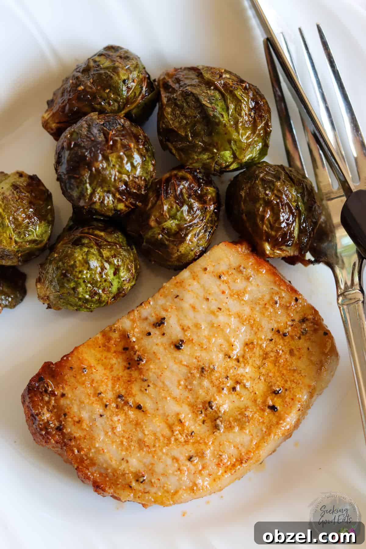 A frozen pork chop cooked in an air fryer served on a white plate with brussels sprouts