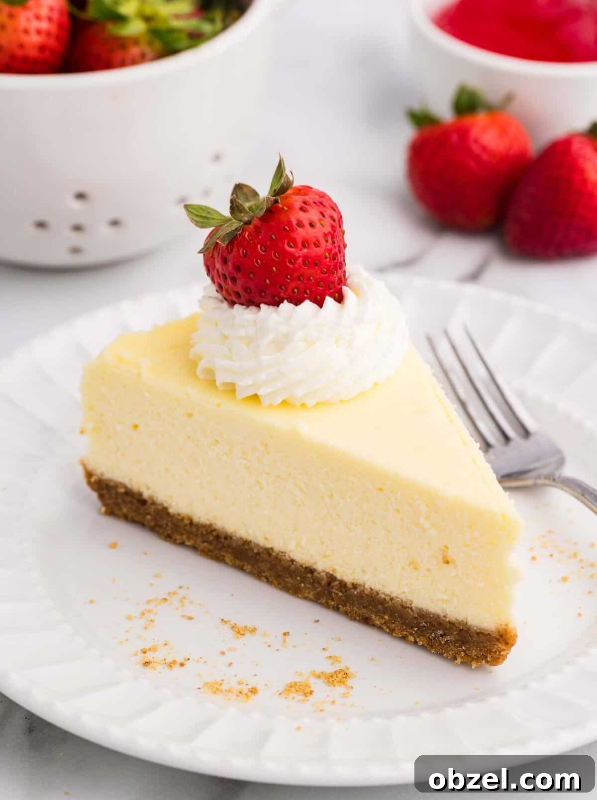 Creamy Loaf Pan Cheesecake Recipe 2 A slice of creamy loaf pan cheesecake with a graham cracker crust, topped with whipped cream and a fresh strawberry, served on a white plate with a fork and strawberries in the background
