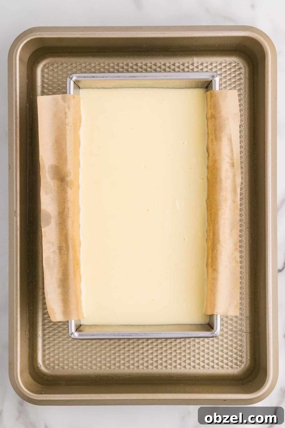 Creamy Loaf Pan Cheesecake Recipe 12 Overhead view of a parchment-lined loaf pan filled with cheesecake batter sitting inside a larger baking pan for a water bath, ready to go into the oven