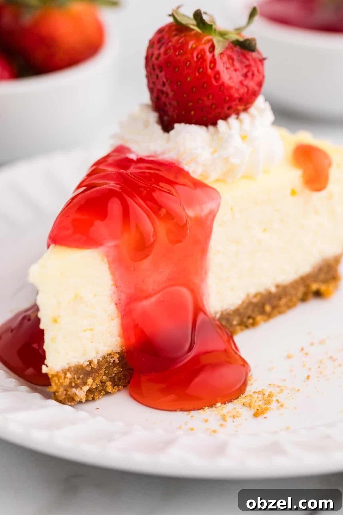 Creamy Loaf Pan Cheesecake Recipe 18 Close-up of a creamy cheesecake slice drizzled with strawberry sauce, topped with whipped cream and a fresh strawberry, served on a white plate