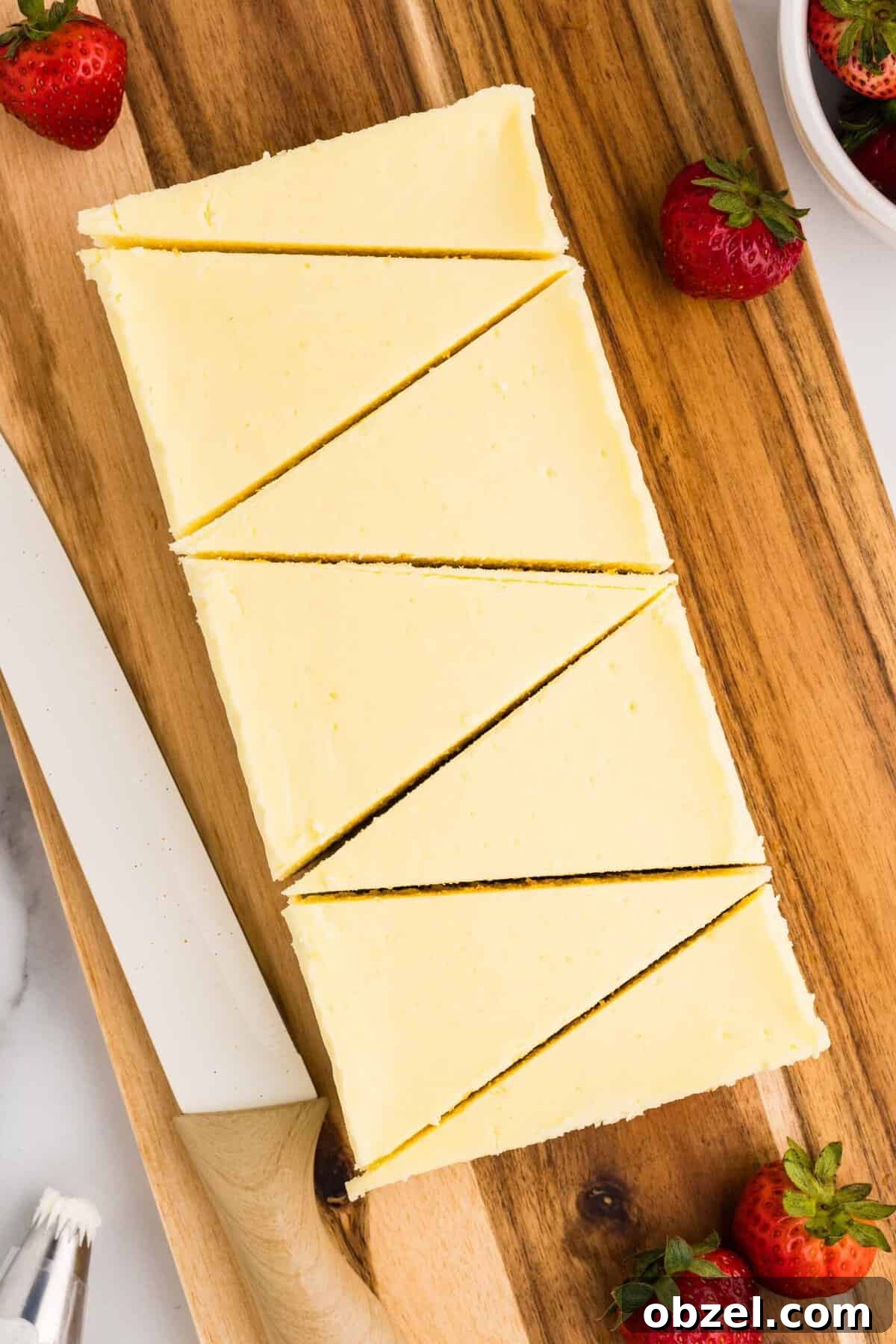 Creamy Loaf Pan Cheesecake Recipe 4 Overhead view of a whole loaf pan cheesecake sliced into triangular pieces on a wooden cutting board, with fresh strawberries scattered around