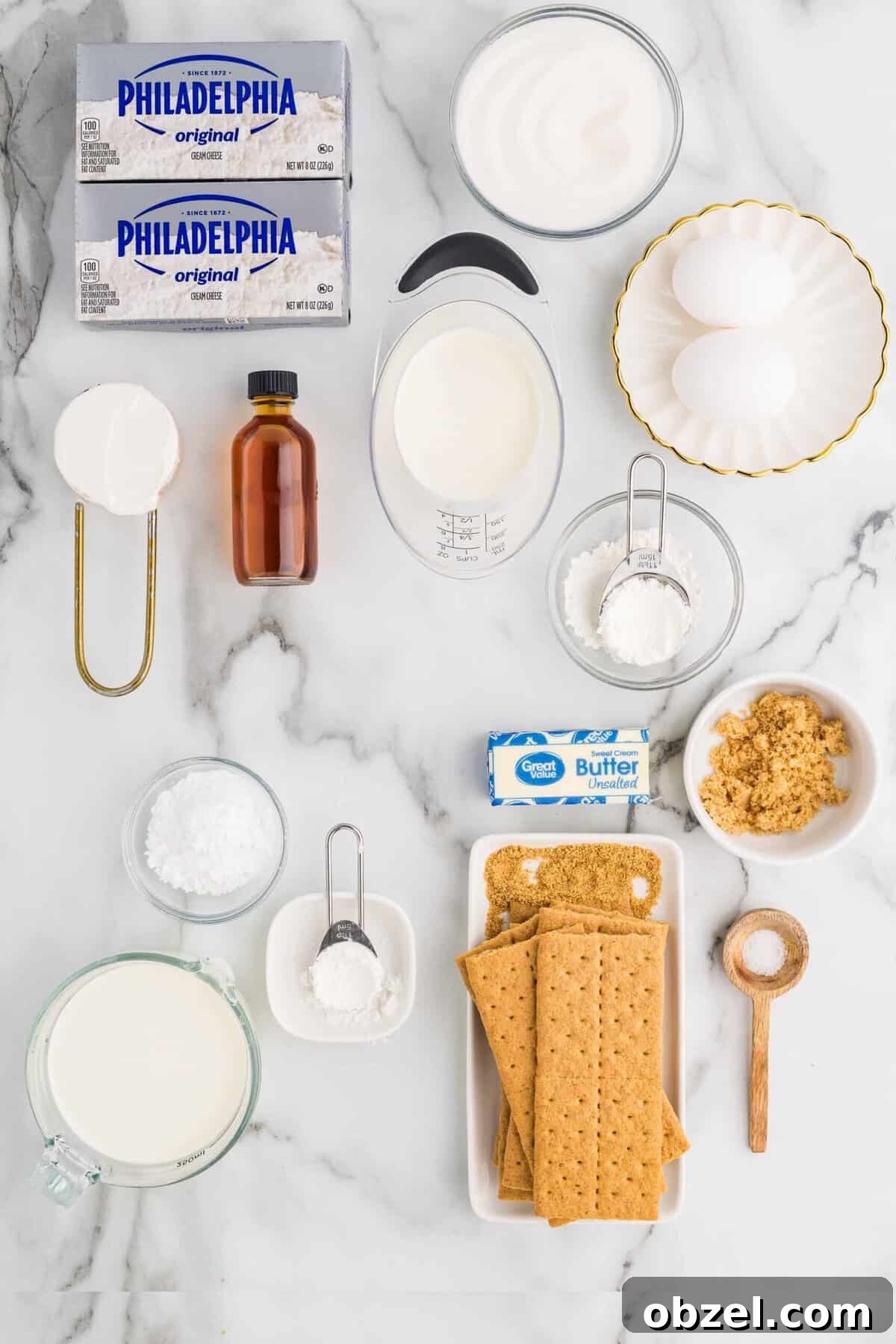 Creamy Loaf Pan Cheesecake Recipe 6 Flat-lay of loaf pan cheesecake ingredients on a marble surface, including Philadelphia cream cheese blocks, sour cream, eggs, vanilla extract, heavy cream, sugar, graham crackers, butter, and cornstarch