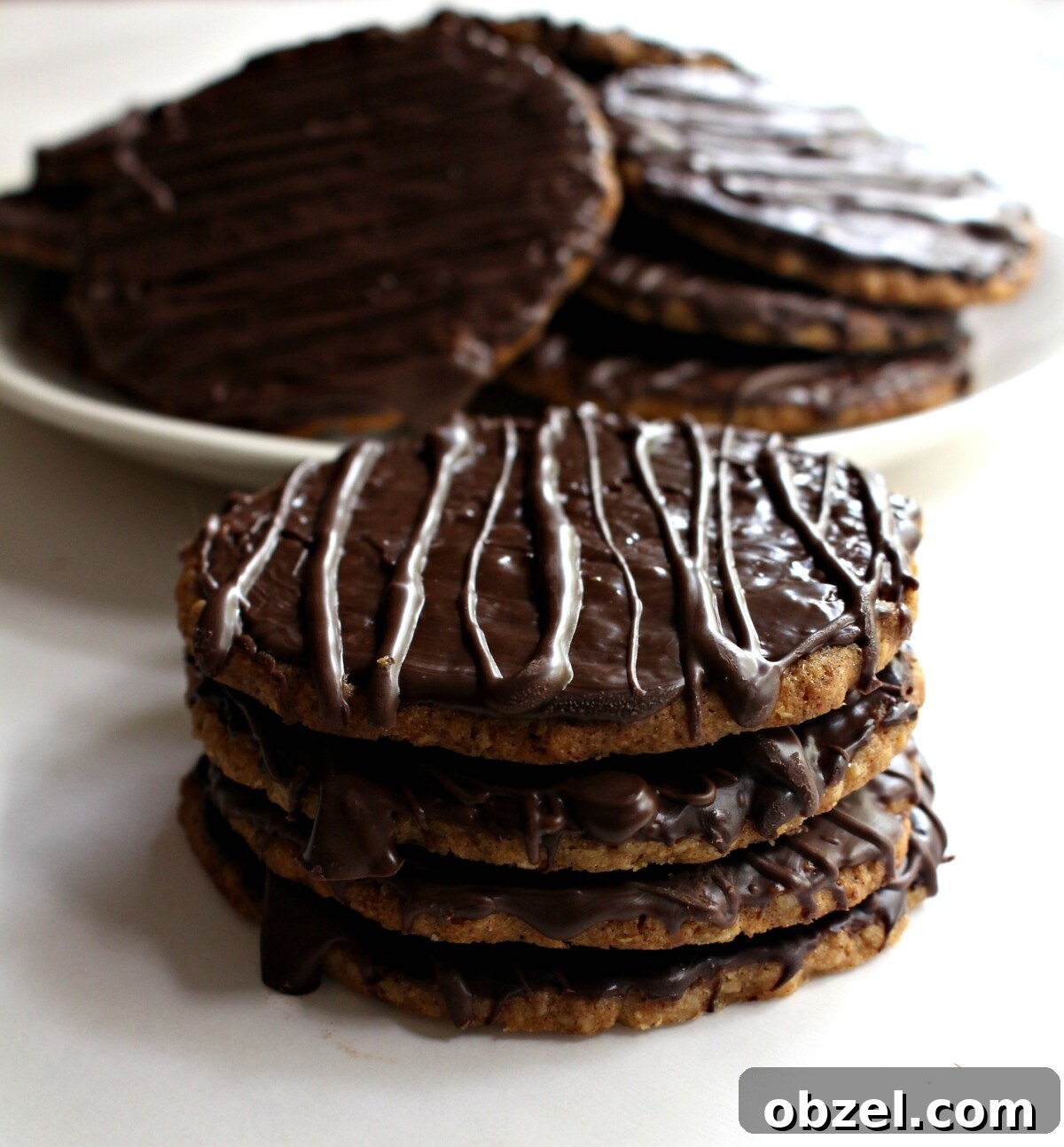 Chocolate Covered Hobnob Oat Cookies Recipe 4 Four cookies in a stack and a white plate of cookies in the background.