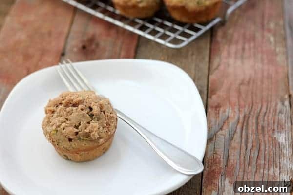 Gluten Free Zucchini Muffins with Streusel Topping 3 Image shows a white plate with a gluten free zucchini streusel muffin on it with a fork. Nearby a cooling rack holds more muffins