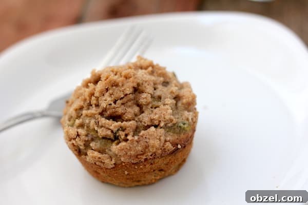 Gluten Free Zucchini Muffins with Streusel Topping 4 Image shows a close up of a gluten free zucchini streusel muffin on a white plate with a fork nearby.