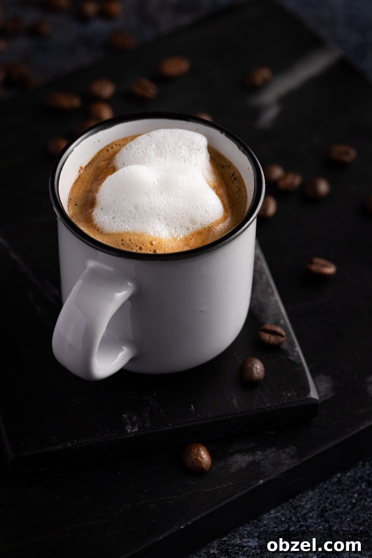 Starbucks Doppio Caffeine Calories and Price 3 Doppio macchiato in a small white cup on a black coaster with coffee beans scattered on the table.