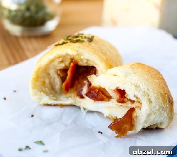 Cheesy Bacon and Pepper Jack Stuffed Crescent Rolls 5 Bacon and pepper jack stuffed crescent roll cut in half on wax paper on a cutting board.