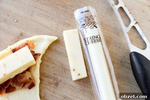 Cheesy Bacon and Pepper Jack Stuffed Crescent Rolls 8 pepper jack string cheese cut into a cube with a knife on a cutting board. and a crescent roll topped with cheese cube and bacon.