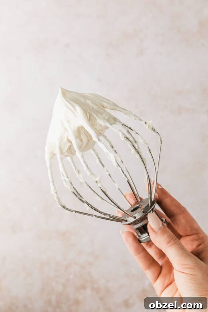Pumpkin Spice Mini Bundt Cakes 15 A hand holding a whisk of cream cheese frosting for pumpkin mini bundt cakes.