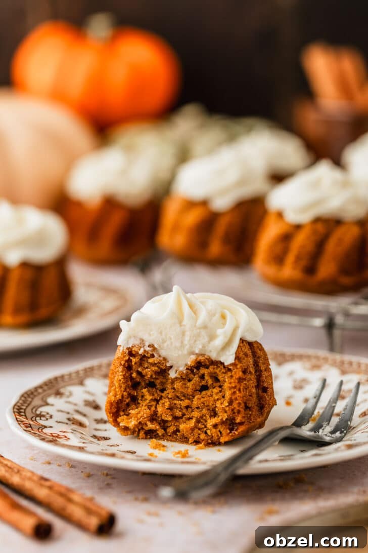 Pumpkin Spice Mini Bundt Cakes 16 A brown plate with a cake on a tan counter next to pumpkins, cinnamon sticks, and a wire rack of pumpkin mini bundt cakes.