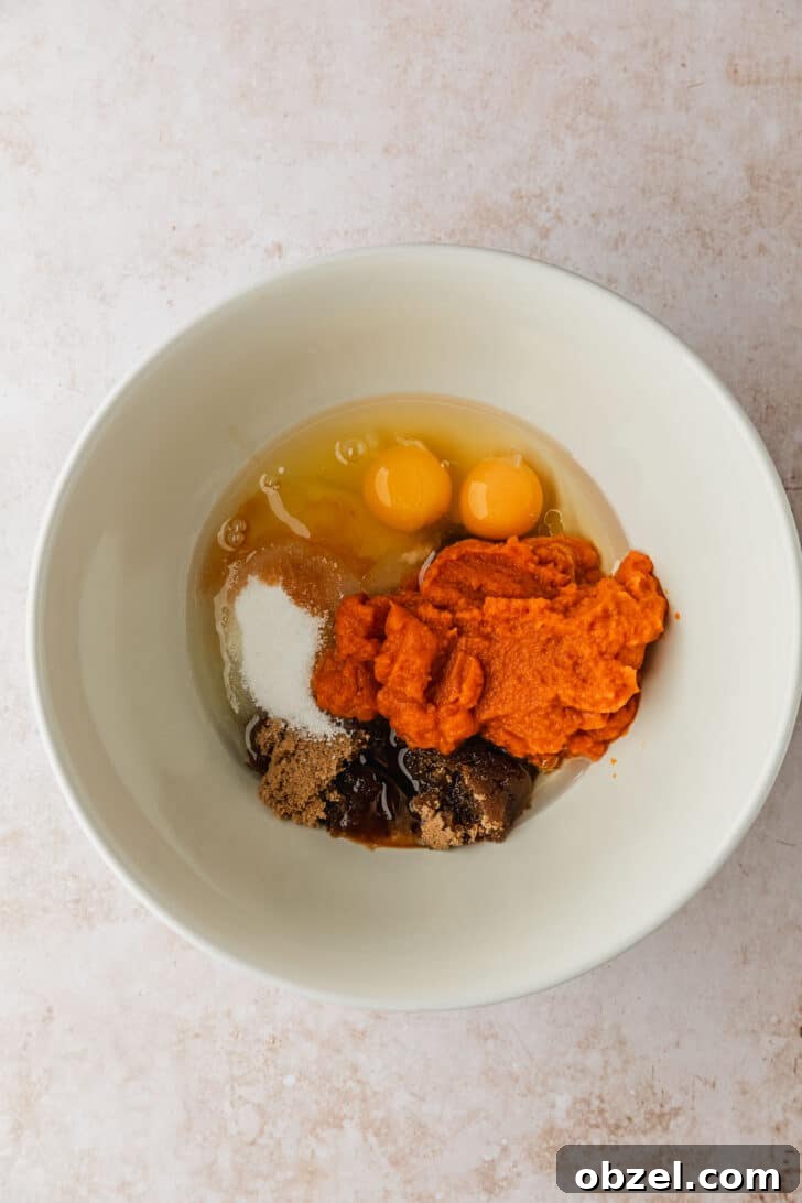 Pumpkin Spice Mini Bundt Cakes 5 A white bowl of pumpkin, eggs, sugar, and oil on a tan counter.