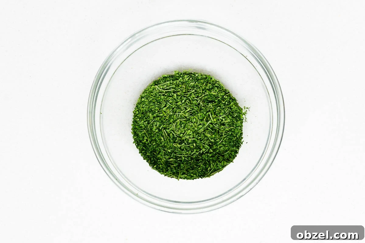 How to Dry Parsley in the Oven for Crisp, Flavorful Herbs 8 Crumbled oven dried parsley with larger stems removed, in a glass bowl viewed from above.