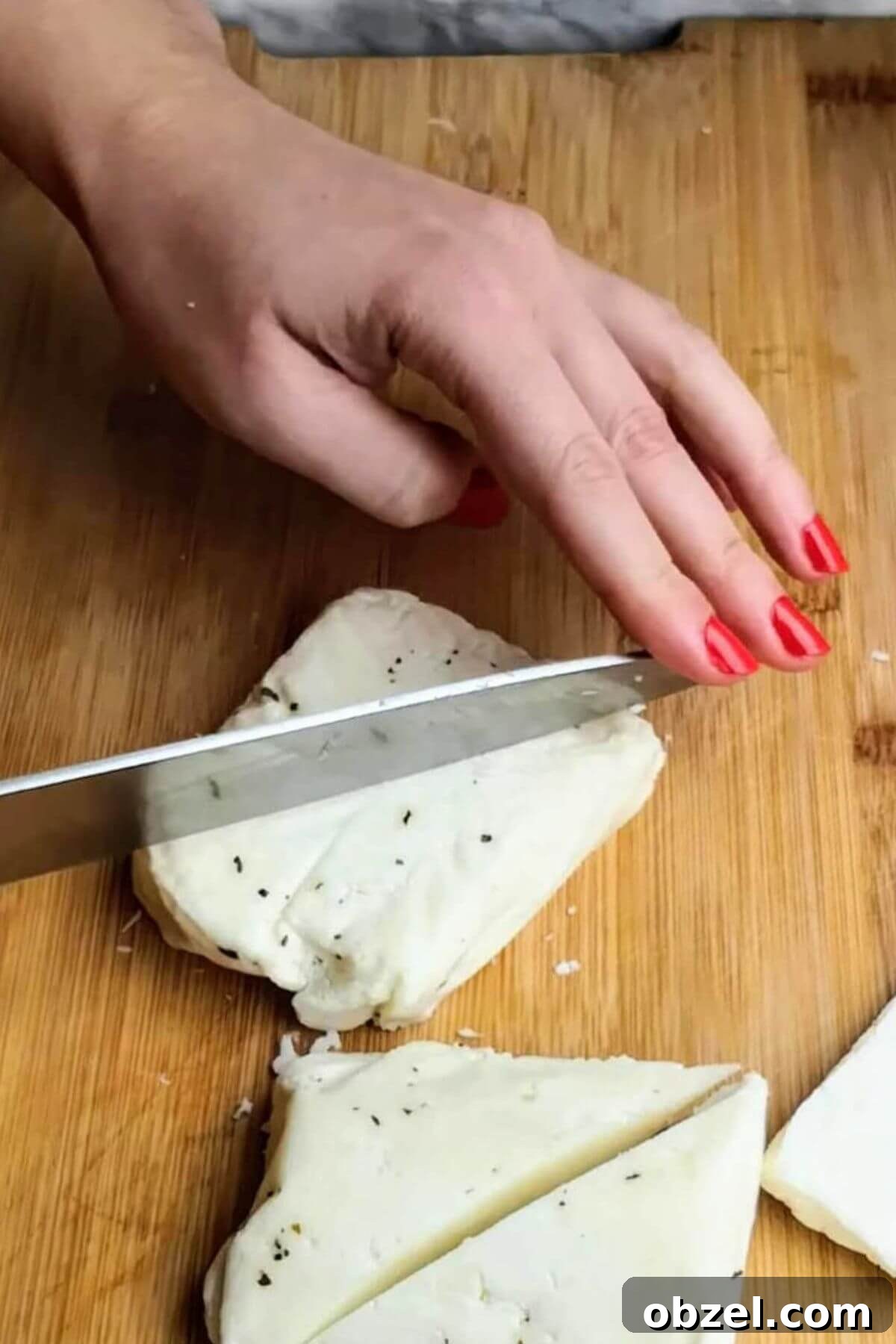 Honey and Harissa Glazed Halloumi Recipe 5 Hand cutting large triangle of halloumi with a knife.