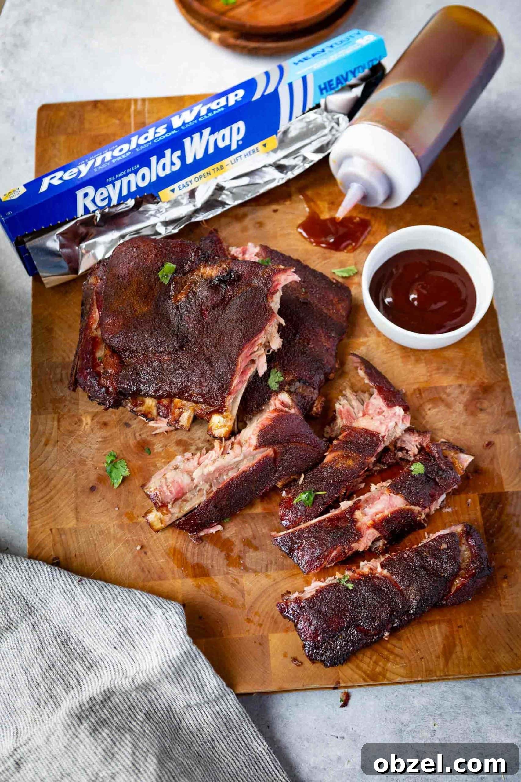 Easy BBQ Spare Ribs a photo of a rack of grilled spare ribs broken apart on a wooden cutting board with barbecue sauce on the side