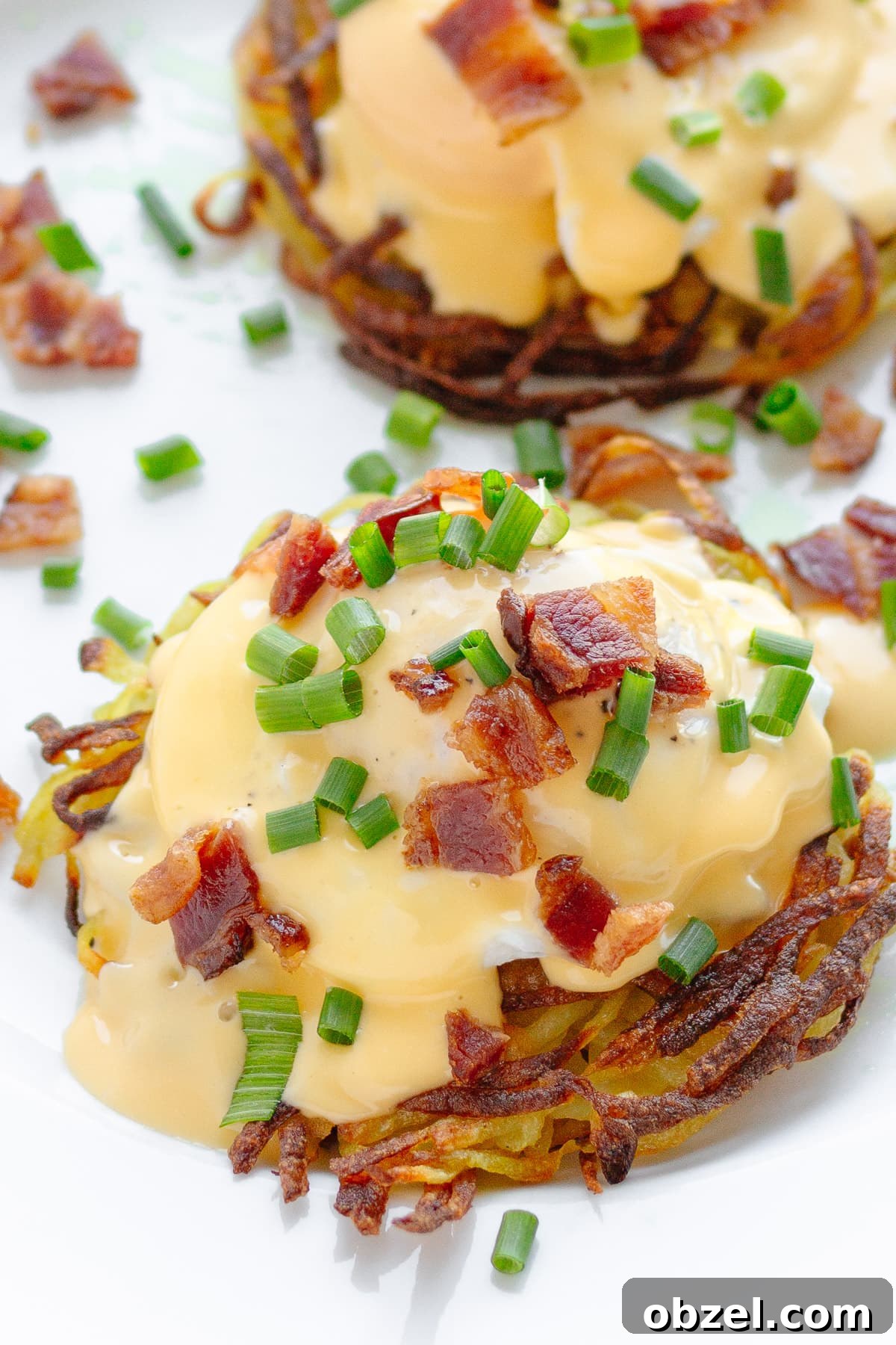 Rosti Eggs Benedict with Crispy Potato Pancakes 3 Two Rosti Eggs Benedict on a white plate garnished with chopped bacon and fresh chives.