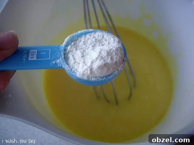 A measuring spoon with flour above the liquid mixture.