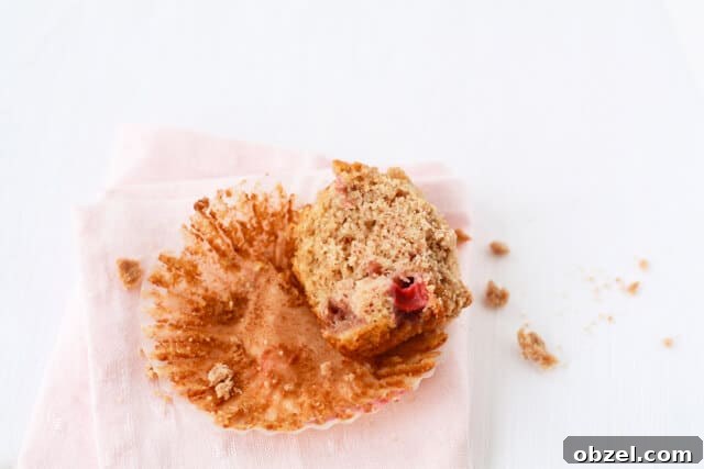 Half of a strawberry rhubarb muffins with crumble topping on a paper liner with a pink napkin 