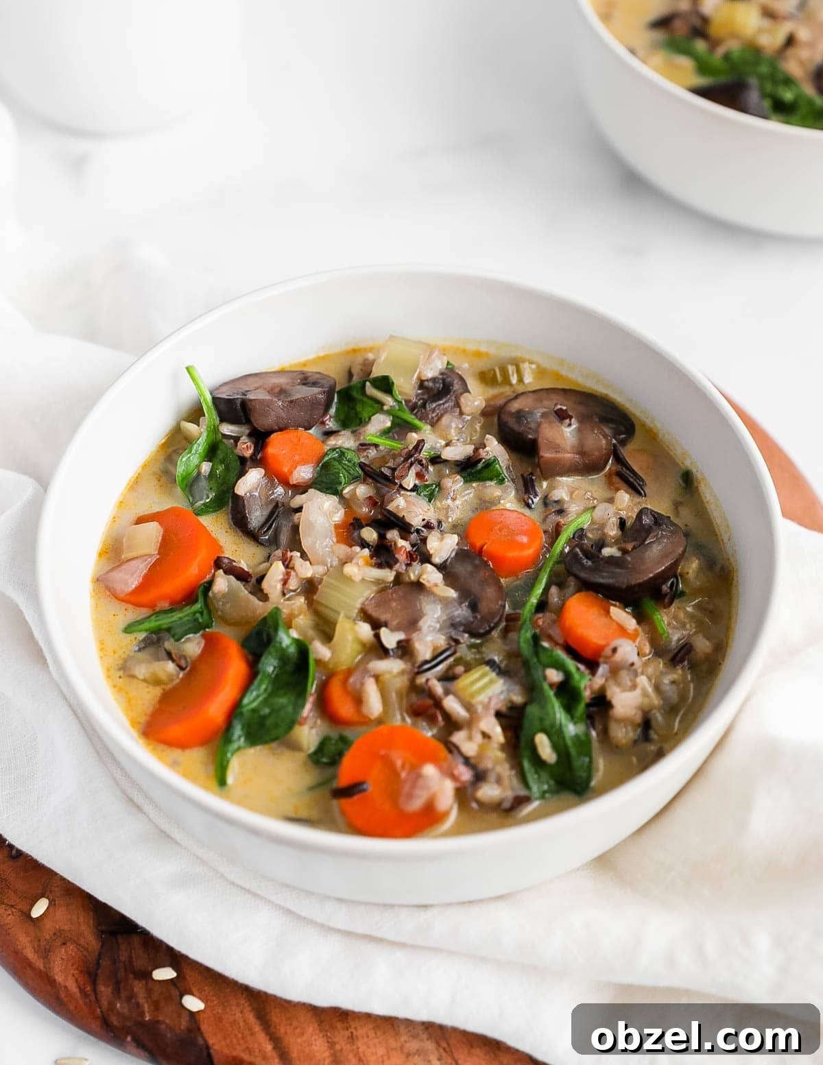 Creamy Wild Rice and Mushroom Soup Recipe 2 A bowl of vegetable and rice soup with mushrooms, carrots, spinach.